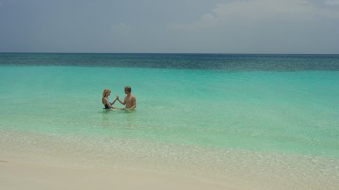 Distant romantic couple wading in ocean and holding hands / Grand Anse Beach, Grenada