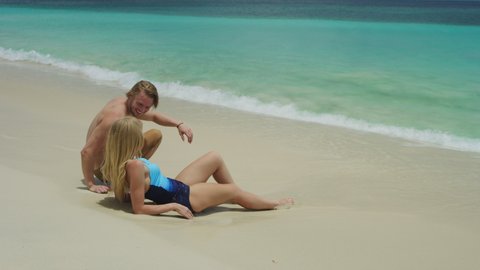 Slow motion of man joining beautiful woman relaxing on ocean beach / Grand Anse Beach, Grenada