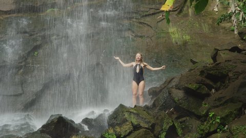 Happy woman standing on rocks under waterfall / Carmel Falls, Grenada