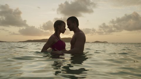 Romantic couple holding hands and kissing in ocean at sunset / Jamesby Island, Tobago Cays, St. Vincent and the Grenadines