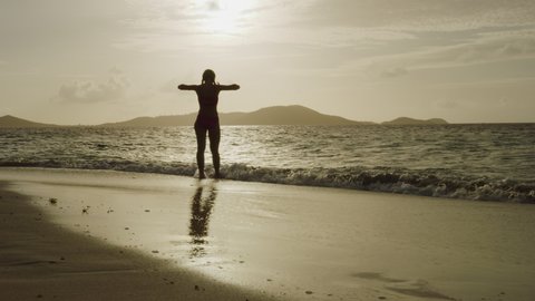 Slow motion of silhouette of woman walking on beach into ocean at sunset / Jamesby Island, Tobago Cays, St. Vincent and the Grenadines