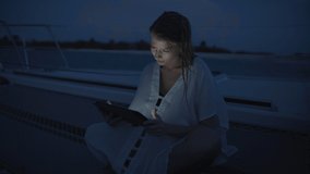 Woman sitting on beach at night watching digital tablet / Tobago Cays, St. Vincent and the Grenadines