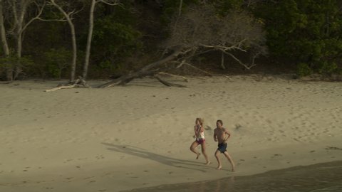 Aerial view of distant couple running on ocean beach / Anse La Roche bay, Carriacou, Grenada