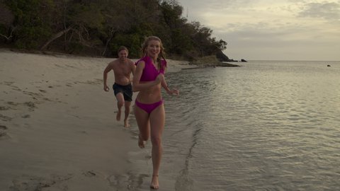 Slow motion tracking shot of man chasing woman on beach then dunking her in ocean / Anse La Roche bay, Carriacou, Grenada
