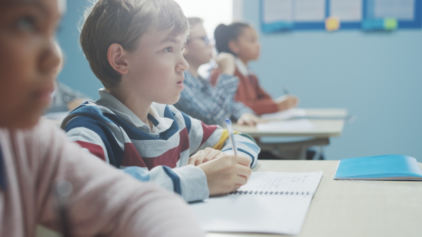 In Elementary School Class: Portrait of Brilliant Caucasian Boy Writes in Exercise Notebook, Taking Test and Writing Exam. Diverse Group of Bright Children Working Diligently and Learning Royalty-Free Stock Footage #1039974377