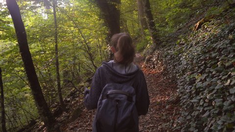 Girl tourist with a backpack walks along a forest trail looking around and admiring the forest beauty