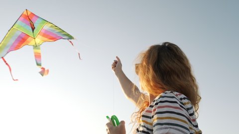Happy woman stands in field and holds kite with tail in strong wind in windy park, red-haired in sunglasses, looks horizon against background of wind turbines and sunset. Lifestyle. Freedom. Relax Stock-video