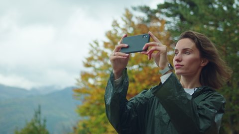 Beautiful happy traveller woman with curly hair in green raincoat shoots video on smartphone sharing with friends enjoying vacation hiking in pyrenees mountains, Freedom Calm Autumn Travel Adventure