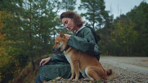 Young Happy Woman Travels with Beloved Shiba Inu Dog Hiking in Pyrenees Mountains, Beautiful girl with wet curly hair enjoying the view sitting and stroking the dog in autumn rainy forest, Cinematic