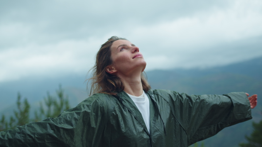 Free Happy Young Hiker Woman in green raincoat looking up with raised arms enjoying calm rainy day in the nature breathing fresh air, hair blowing in wind, People Mountains Freedom Concept, Happiness | Shutterstock HD Video #1039980731