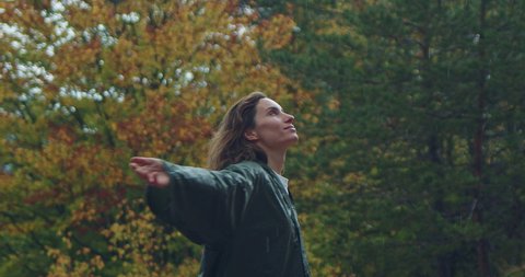 Free happy woman with wet curly hair in green raincoat arms up praising freedom in autumn forest in the mountains, Carefree young woman enjoying breathing freely fresh air, Cinematic Shot