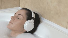 Woman taking a bubble bath in bathroom at home and wearing headphones.Wireless Freedom With Bluetooth Technology concept