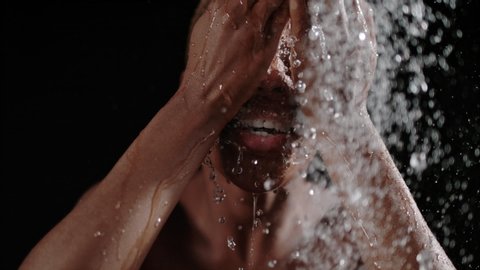 Beautiful black woman having a shower in slow motion. Head of a black woman under a shower on a black background