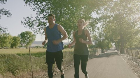 Tracking shot of couple running on path in park / Saratoga Springs, Utah, United States