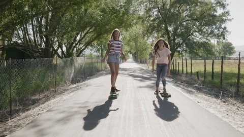 Tracking shot of girl on skateboard photographing friend then posing for cell phone selfie / Saratoga Springs, Utah, United States