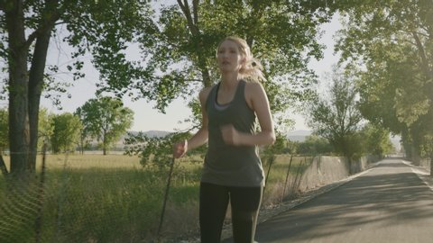 Tracking shot of woman running on path in park / Saratoga Springs, Utah, United States