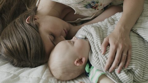 High angle close up of mother and baby son cuddling and napping on bed / American Fork, Utah, United States