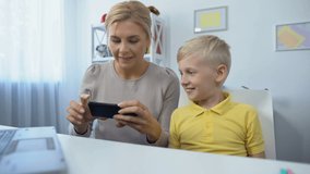 Happy mother and son playing games on smartphone together, having fun, app