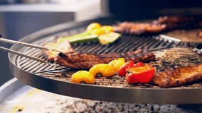 Preparing delicious food on rotating barbecue grid. Turning around ribs and vegetables with cooking forceps while circular grid for bbq is moving around its axis