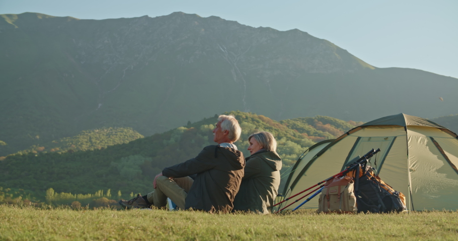 Mature caucasian couple travelling together after retirement, taking a rest on top of mountain, enjoying the view and talking - pension, recreational pursuit, tourism concept 4k