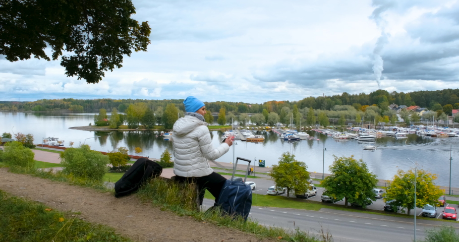a young woman takes pictures on the phone the beauty of the nature of the city of Lappeenranta in Finland. Autumn nature of Finland. A woman sits on a hill and looks down. proress 4K 25P slow motion