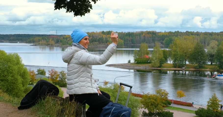 a young woman takes pictures on the phone the beauty of the nature of the city of Lappeenranta in Finland. Autumn nature of Finland. A woman sits on a hill and looks down. proress 4K 50P