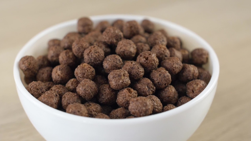 Dry breakfast cereals chocolate and wheat balls in whhite plate with milk pouring on it. Close up slow motion food footage. Healthcare morning sweet sneak.