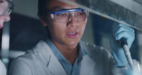 Close up shot of Chinese male scientist is analyzing with a pipette a liquid to extract the DNA and molecules in the test tubes in laboratory.