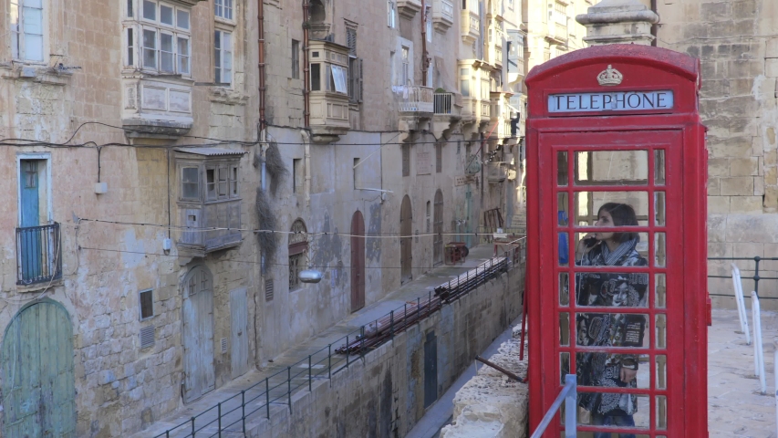 portrait of woman talking on the phone in a red telephone booth in a small village