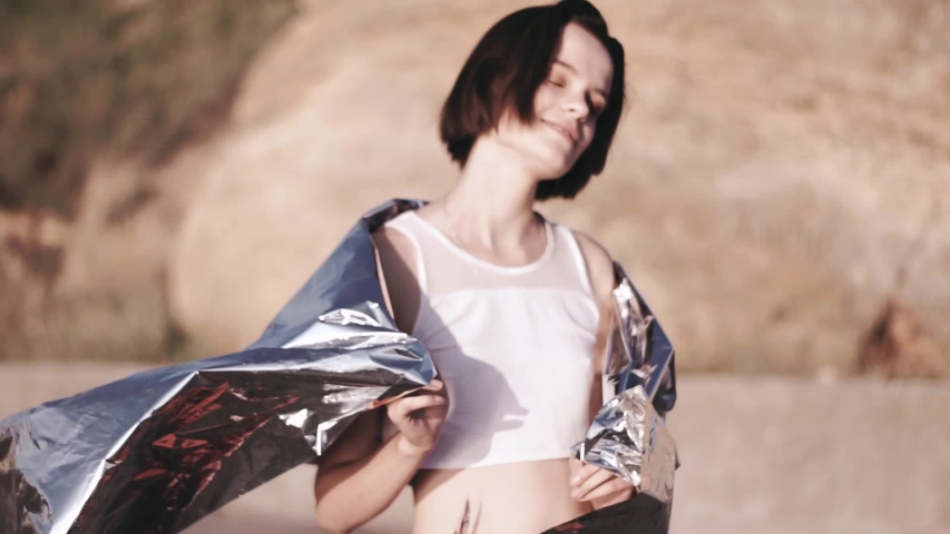 Fashion photo session and video of a young beautiful woman with foil on sunrise.Vogue style concept. hand and legs on foil.