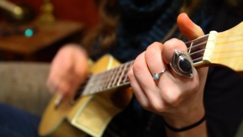 Close up of a young girl's hands learning how to play ukulele sitting in a sofa in her living room - fixed angle