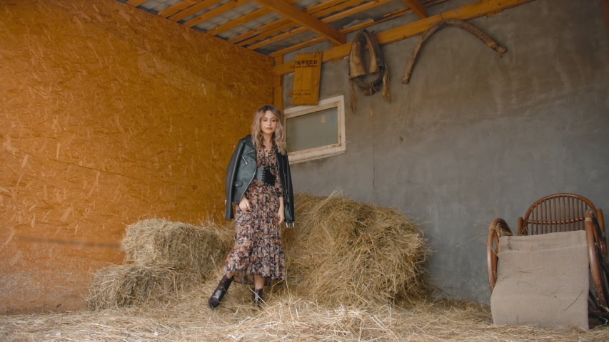 Low angle of stylish female in dress kicking hay and spinning while dancing in shabby shed on ranch