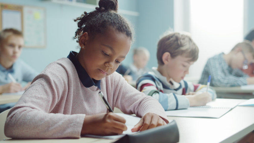 In Elementary School Class: Portrait of a Brilliant Black Girl with Braces Writes in Exercise Notebook, Smiles. Junior Classroom with Diverse Group of Bright Children Working Diligently and Learning  Royalty-Free Stock Footage #1040038280