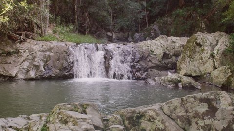 Rising above past rocks to reveal beautiful waterfalls surrounded by forest in Australia. Wide shot on 4k RED camera.