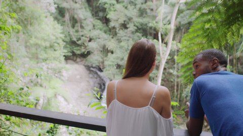 Two millennial friends leaning on railing in front of small waterfall in an Australian rainforest by safety railing during daytime. Medium shot with camera zoom on 4k RED camera.