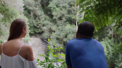 Two millennial friends leaning on railing in front of small waterfall in an Australian rainforest by safety railing during daytime. Medium shot on 4k RED camera.