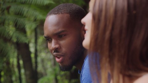 Interracial couple talking and laughing in an Australian rainforest through shaded green dense treebed during daytime. Closeup shot on 4k RED camera.
