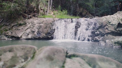 Pan across rocks revealing beautiful waterfalls surrounded by lush forest in Australia. Wide shot on 4k RED camera.