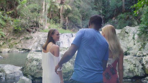 Three young beautiful friends hikers walking, hiking along river bed in lush forest, finding waterfalls. Wide shot on 4k RED camera.