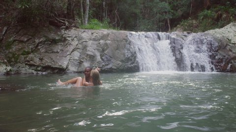 Young beautiful couple swimming in secluded river near waterfall. Wide shot on 4k RED camera.