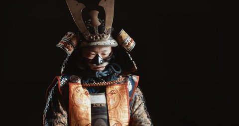 Man in traditional japanese samurai clothing is looking at camera and demontrating his katana sword, isolated on black background - culture, tradition, martial arts concept 4k footage