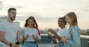 Man opening bottle of champagne with female friends. Group of happy young people laughing, having fun. celebrating birthday at party on rooftop. 4k slow motion raw video footage 60 fps