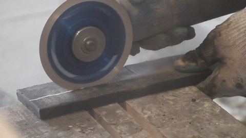 A man 's hand cuts off pieces of ceramic tile using a corner grinding machine. Cutting ceramic tiles with dust and black smoke on the construction site.