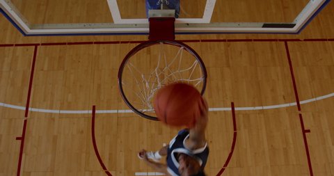 OVERHEAD HIGH ANGLE JIB SHOT African American black college male basketball player practicing dunks alone on the indoor court. 4K UHD 50 FPS SLOW MOTION RAW Graded footage