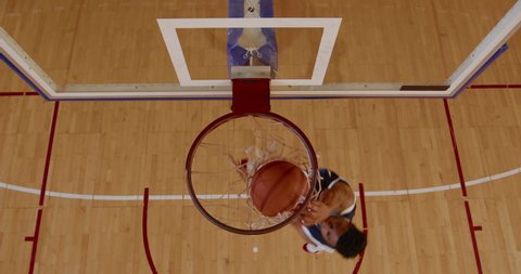 OVERHEAD HIGH ANGLE JIB SHOT African American black college male basketball player practicing dunks alone on the indoor court. 4K UHD 50 FPS SLOW MOTION RAW Graded footage