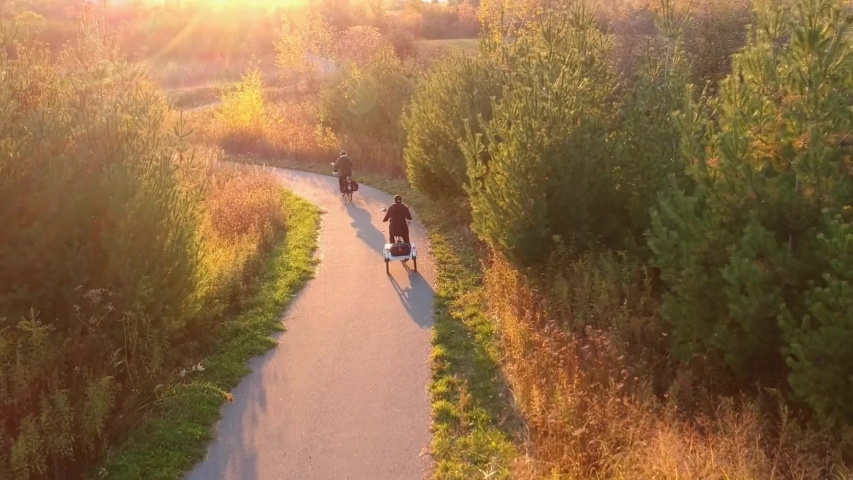 Travelers, woman and man cycling on the bikes or riding bicycles in Fall or Autumn rural park at golden hour sunset. Vacation activity, aerial view from above over orange, yellow and green trees.