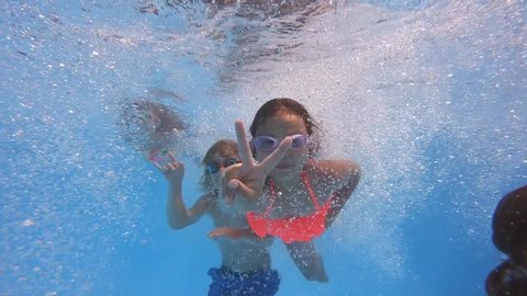 Underwater view of having fun group of children jumping and diving into swimming pool at pool party in summer sunny day. Happy children. Slow motion. Childhood, friendship, vacation concept