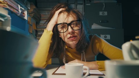 Stressed businesswoman working late at night in the office, she had too many cups of coffee and feels exhausted