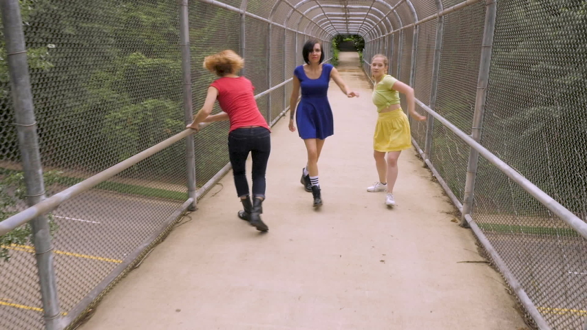 Three women dancing and moving forward on a pedestrian bridge in slow motion - stabilized shot
