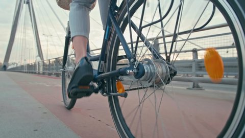 Close up of Bike Wheels and Female Feet in Casual Shoes Cycling in City on Bridge in the Autumn Morning. Urban Cycle Chic and Ecological Transportation by Bike. 4K Close up Low Angle Tracking Shot